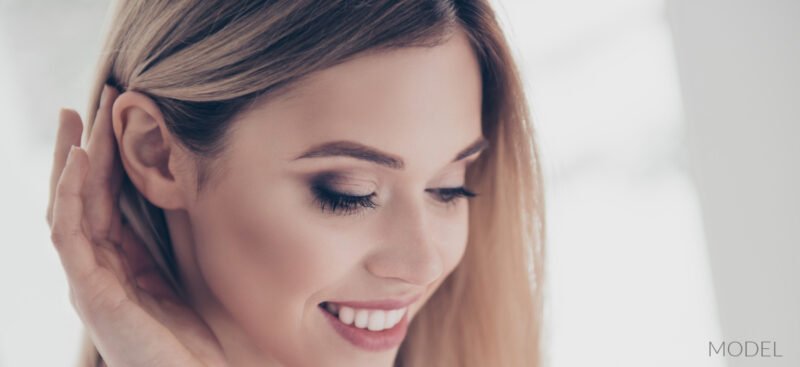 Close up of pretty, smiling blonde tucking hair behind her ear