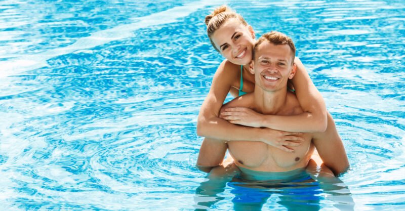 Smiling man giving piggyback ride to woman in the pool