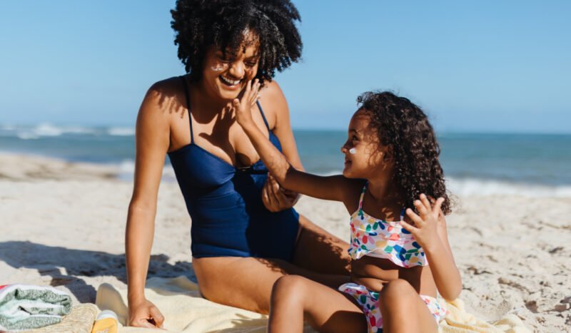 A woman in a blue bathing suit on the beach with her young daughter playing in the sand