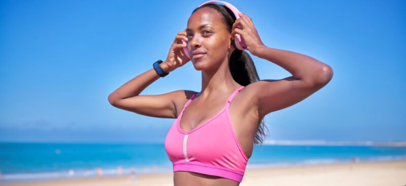 Young African American woman wearing a pink sports bra and headphones while running on the beach