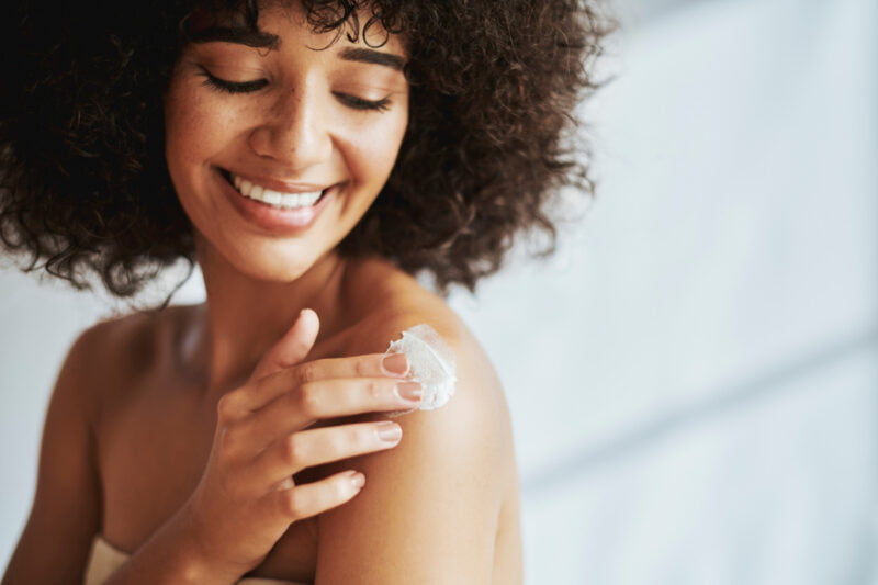 Woman smiling and applying SPF on her shoulder