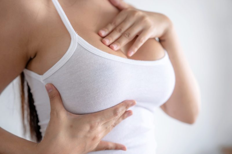 Faceless woman lifting breasts wearing white tank top